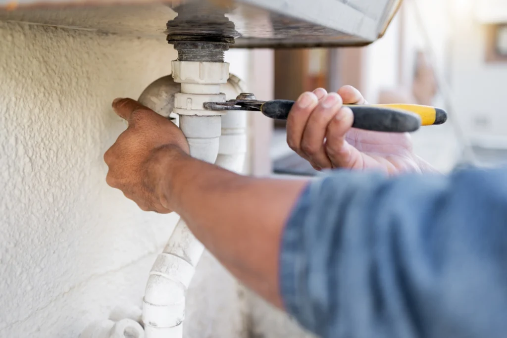 Plumber tightening a white PVC drain pipe under a sink with a wrench during drain pipe repair in Greenville, SC