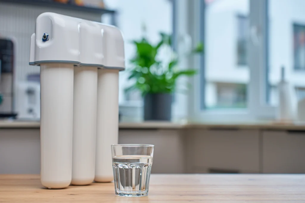 Three-stage home water filtration system next to a glass of clean filtered water