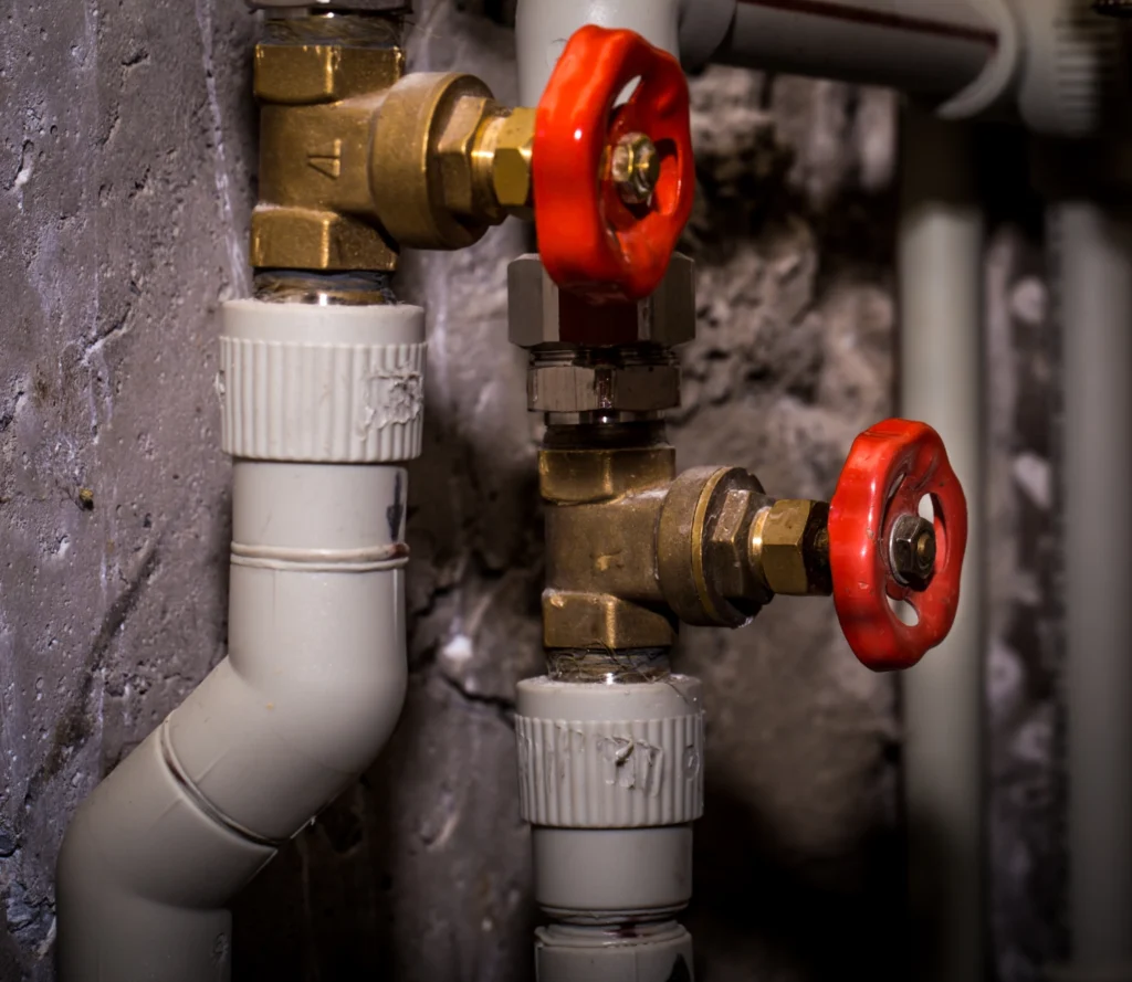 Brass water shutoff valves with red handles on white plastic supply pipes